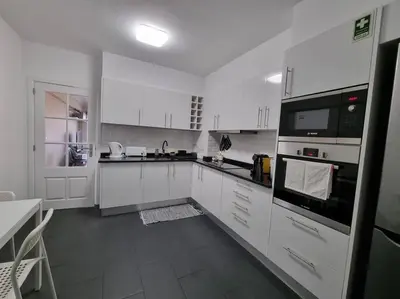 a white kitchen with white cabinets and a black appliance at Olimpia Gardens View by Rentallido in Funchal