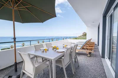 a white table and chairs on a balcony with the ocean at Esterinha's Ocean Apartment by GALMI in Jardim do Mar