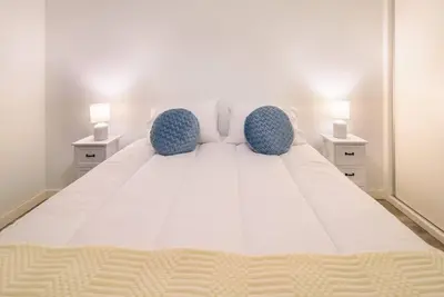 a large white bed with two blue chairs and two lamps at Casa da Clara by MTH in Caniço