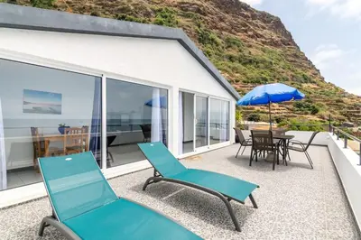 a patio with chairs and a table and an umbrella at Esterinha's Sunset Apartment by GALMI in Estreito da Calheta