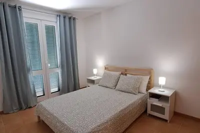 a bedroom with a bed with two night stands and windows at Casa das Lombas in Vila Baleira