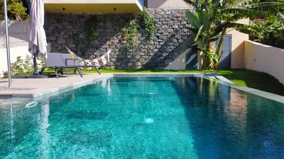 a swimming pool with a table and a chair in front of a house at Serenity Valley Escape by LovelyStay in Ribeira Brava