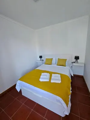 a white bedroom with a large bed with yellow sheets at Apartamento Costa Norte in Porto Moniz
