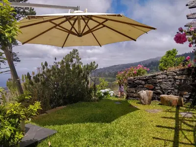 a yellow umbrella in a yard with a stone wall at Achadinha - Mountain Cottage in Arco da Calheta