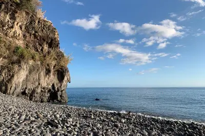a rocky beach with people swimming in the ocean at Baldeia - Oceanfront Apartments in Ponta do Sol