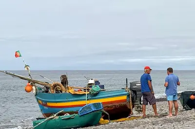 two men standing next to a boat on the beach at Baldeia - Oceanfront Apartments in Ponta do Sol