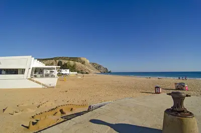 a sandy beach with a building and the ocean at LGS62 V3 casa e jardim a 100mts praia da Luz in Luz