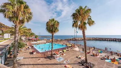 a group of people sitting around a swimming pool with palm trees at Neves GuestLoft by Madeira Holiday Rentals in Ribeira Brava