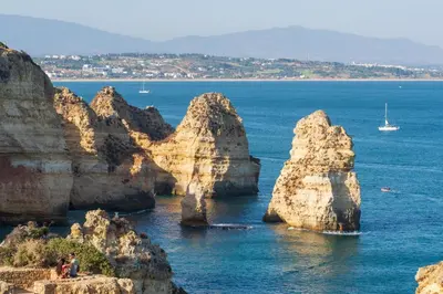 a group of rocks in the ocean with a boat at Porto de Mos 86 by Destination Algarve in Lagos