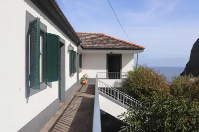 a white house with green shutters and the ocean at Casa da Avo Rosa in São Vicente
