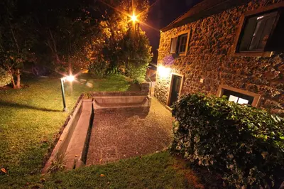 a stone building with a bench in a yard at night at Casa do Ribeirinho in Porto Moniz