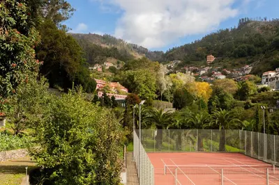 a tennis court on a hill with houses and trees at BIO Hotel - Hotel Quinta da Serra in Estreito de Câmara de Lobos
