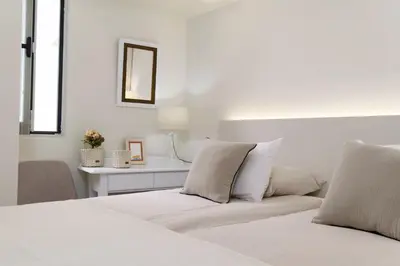 a white bedroom with a bed and a table at Apartamentos do Mar - Pikis Flat in Funchal
