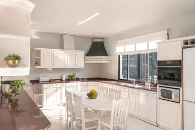 a kitchen with white cabinets and a white table and chairs at Casa Coelho in Ponta do Sol