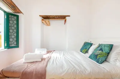 a bedroom with a bed with white sheets and blue pillows at Da Casa Sesta in Sagres
