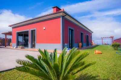 a red building with a palm plant in front of it at Villa Rosa in Porto Moniz