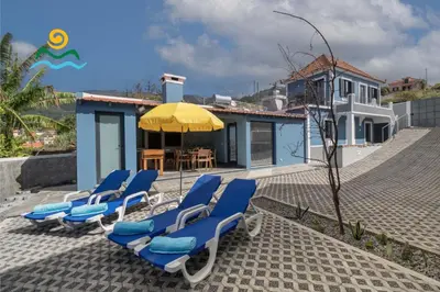 a group of blue lounge chairs and an umbrella at Calheta beautiful character cottage Villa Loreto in Arco da Calheta