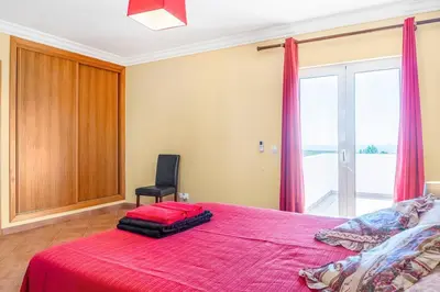 a bedroom with a red bed with a chair and a window at Moradia com piscina e vista Mar in Aljezur