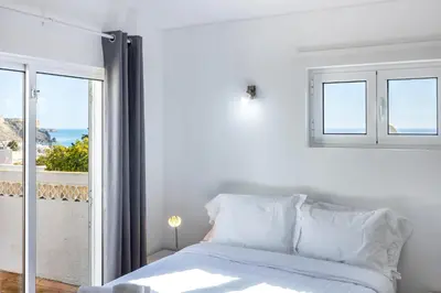 a white bedroom with a bed and a view of the ocean at Casa Coruja in Luz