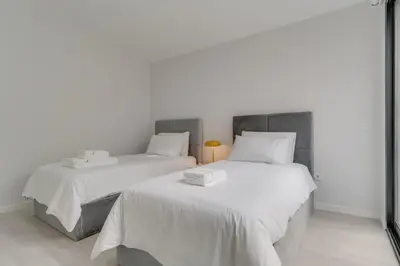 two beds with white sheets in a white room at Graça House in Machico