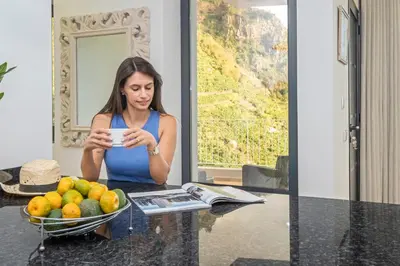 a woman sitting at a table with a bowl of fruit at Stunning view set in nature - Recanto of the sea in Ponta do Sol