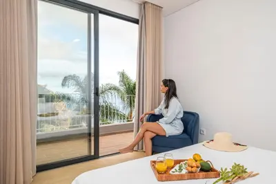 a woman sitting in a chair in a room with a window at Stunning view set in nature - Recanto of the sea in Ponta do Sol