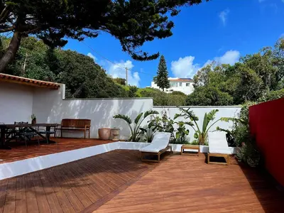 a patio with white chairs and a table and trees at Casa das Escadinhas in Budens