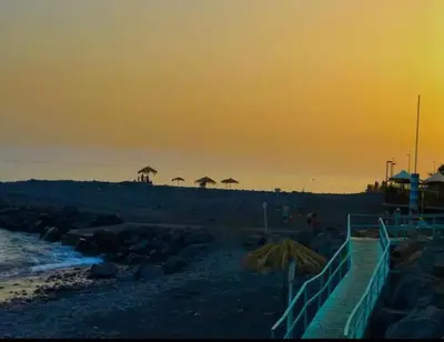 a beach with umbrellas and the ocean at sunset at Praia Formosa Ocean View - Funchal in Funchal