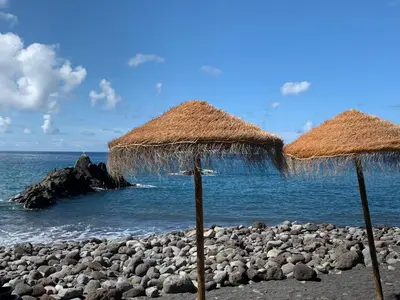 two straw umbrellas on a beach near the water at Praia Formosa Ocean View - Funchal in Funchal