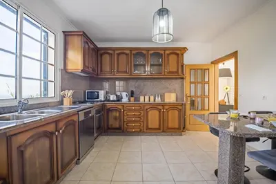 a kitchen with wooden cabinets and a large window at Sunny House by Homie in Canhas