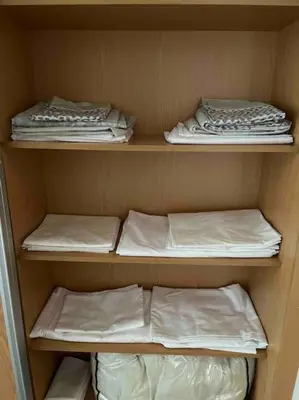 a closet with three shelves with white sheets and pillows at Moradia com piscina no Caniço in Caniço
