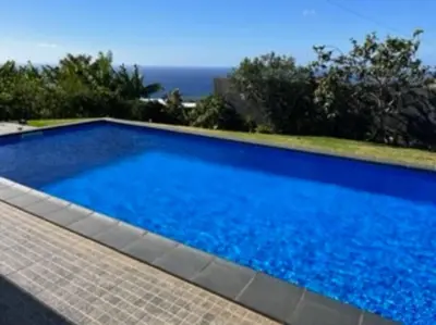 a large blue swimming pool with the ocean in the background at Moradia com piscina no Caniço in Caniço