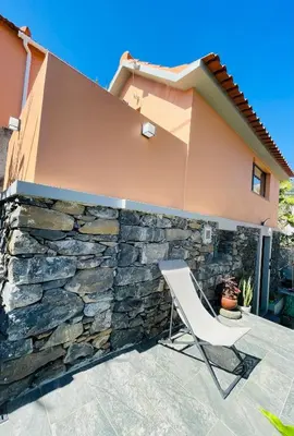 a patio with a stone wall and a white chair at Cozy House in Funchal