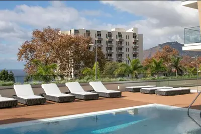 a row of lounge chairs and a swimming pool on a building at Apartamento Zona Turística in Funchal