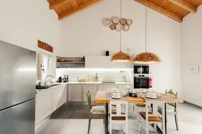 a kitchen with white cabinets and a wooden table with chairs at Casa elegante em Vila tranquila in Barão de São Miguel