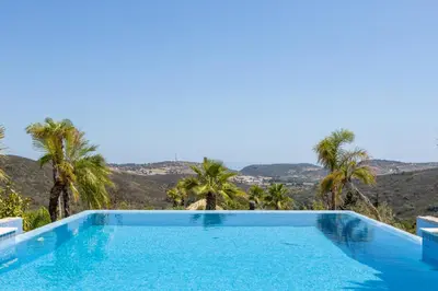 a swimming pool with palm trees and a mountain in the background at Villa Surga, a luxurious and exclusive romantic villa in the Algarve in Budens