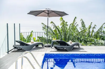 a swimming pool with two chairs and an umbrella at Blue Ocean Villa in Ponta do Sol