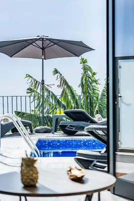 a pool with chairs and an umbrella and a table at Blue Ocean Villa in Ponta do Sol