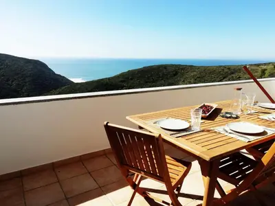 a wooden table and chairs on a balcony with the ocean at Varandas Guest Apartment in Aljezur