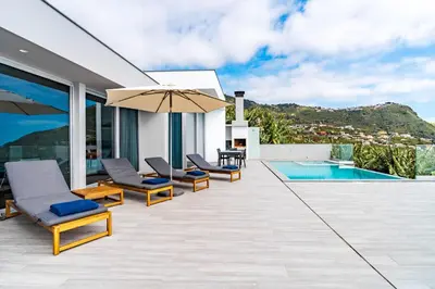 a patio with chairs and an umbrella next to a swimming pool at Villa Anita ,beautiful sunset in Arco da Calheta