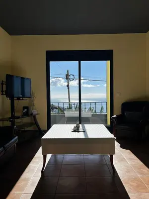 a living room with a table and a large window at Fernanda's House in Ribeira Brava