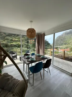 a living room with a table and chairs and a large window at The Green Valley House in São Vicente