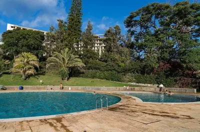 a swimming pool in a park with trees and a building at Caracas Escape by LovelyStay in Funchal