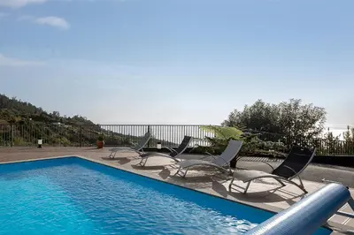 a swimming pool with chairs and the ocean in the background at Villa Panorâmica III in Arco da Calheta
