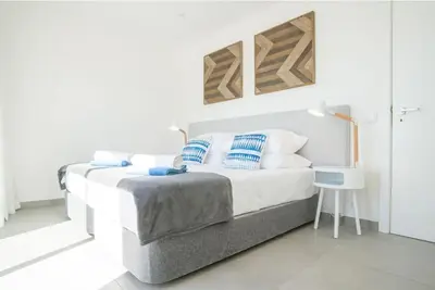 a white bedroom with a bed with blue and white pillows at Casa Vista da Praia in Luz