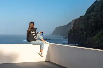 a woman sitting on a wall taking a picture of the ocean at Casa do Terreiro by An Island Apart in São Vicente