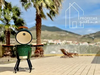a green trash can sitting on a sidewalk with palm trees at Profetas GuestHouse in Porto Santo
