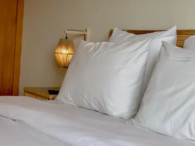 a bed with white pillows and a table with a lamp at Profetas GuestHouse in Porto Santo