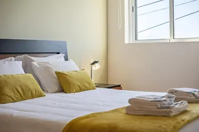 a bed with white sheets and yellow pillows and a window at Canico City Center by Zest and Guest in Santa Cruz