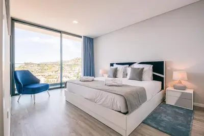 a white bedroom with a large bed and a blue chair at Villa Ocean Haven by AH in Ribeira Brava